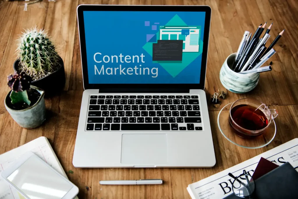 Imagem de um notebook mostrando a mensagem 'Content Marketing' na tela, com elementos de escritório, plantas e uma xícara de chá ao redor, destacando tendências e formatos de vídeo virais no TikTok e Reels para o marketing de conteúdo.