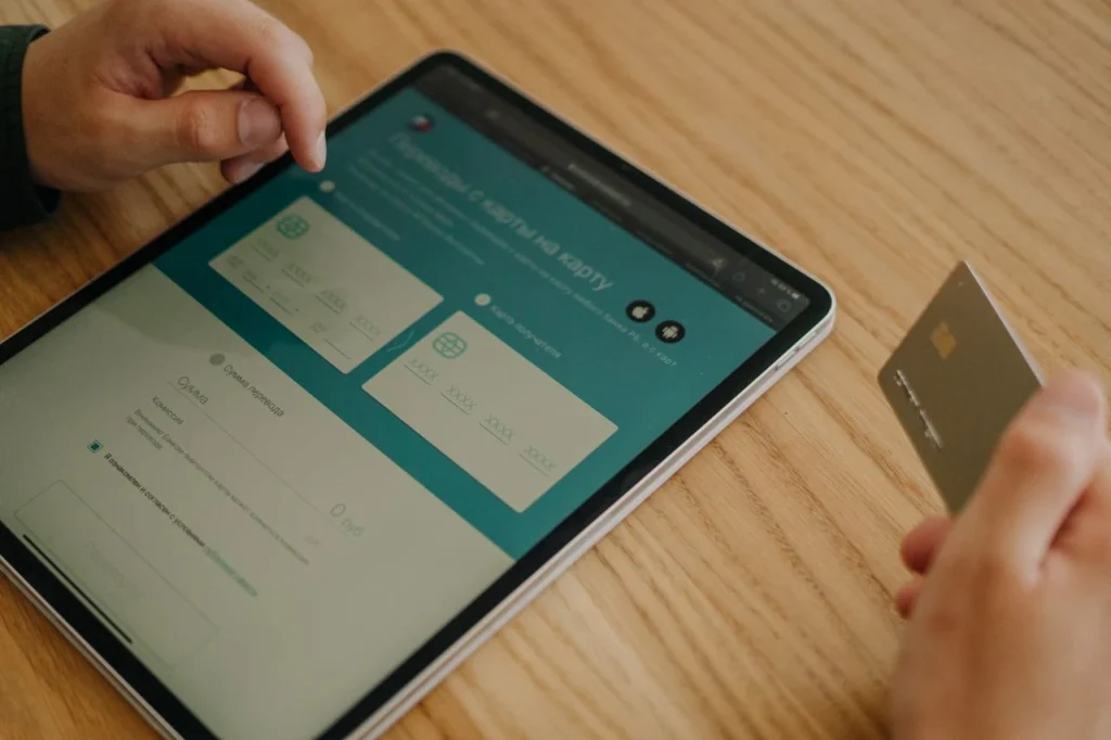 Pessoa usando tablet para configurar pagamento e logística no e-commerce, com cartão bancário na mesa e seleção de etapas de compra e envio