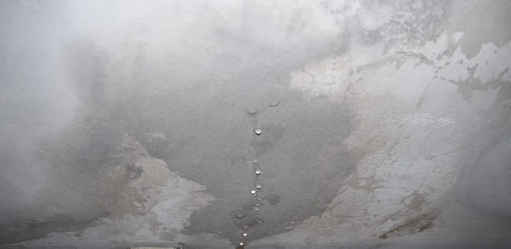 Parede interna com grande mancha de umidade e marcas de infiltração, com descascamento do reboco e pontos de gotejamento no teto, indicando possível vazamento ou condensação.