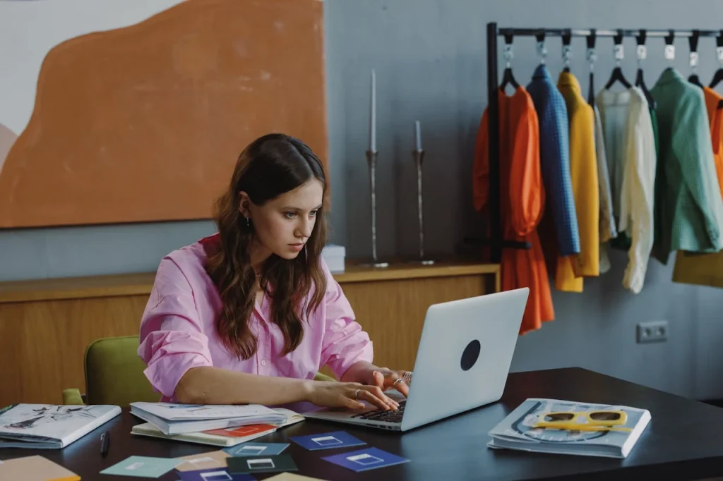 Jovem estudante em escritório com notebook e materiais de estudo sobre a mesa, enquanto ao fundo há casacos pendurados em um ambiente de trabalho, ilustrando por que cursos livres online se tornaram aliados da qualificação profissional.